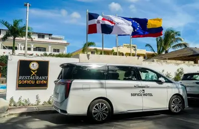 a white van parked in a parking lot with two flags at Soficu Hotel El Edén Dominicus in Bayahibe