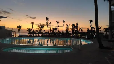a pool with palm trees and a sunset in the background at Apartamentos y habitaciones sol dominicus SOLO ADULTOS in La Laguna