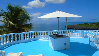 a pool with an umbrella and chairs and the ocean at Guesthouse Villa La Isla in La Romana