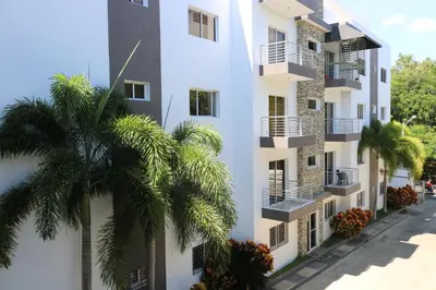 a white building with palm trees in front of it at Apartamento Amueblado Amplio Tranquilo Privado Como tu lo Mereces in Santiago de los Caballeros