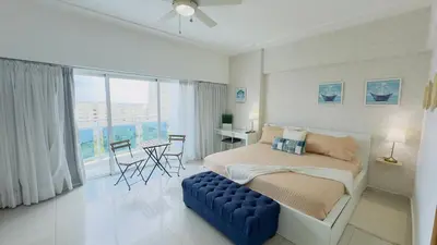 a bedroom with a bed and a blue ottoman in front of a window at Elegante Aqua Marine Apartamento Juan Dolio in Juan Dolio