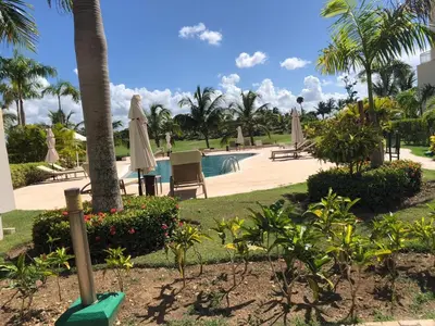 a resort pool with umbrellas and chairs and palm trees at Beautiful One Bedroom unit with pool and Beach club in a Golf Project in Punta Cana
