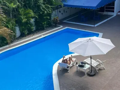 two people sitting in chairs and an umbrella next to a pool at Calypso Beach Hotel in Boca Chica