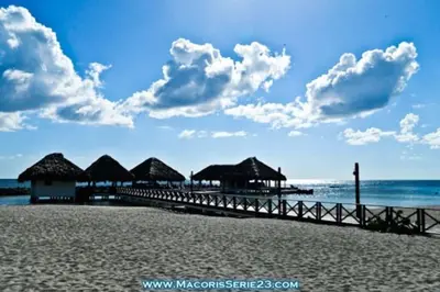 a pier on a beach with huts and the ocean at Elegante Blue Marine Apartamento Juan Dolio in Juan Dolio