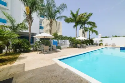 a swimming pool with chairs and umbrellas next to a building at Blue Boat Lindo Apartamento en Playa Juan Dolio in Juan Pedro