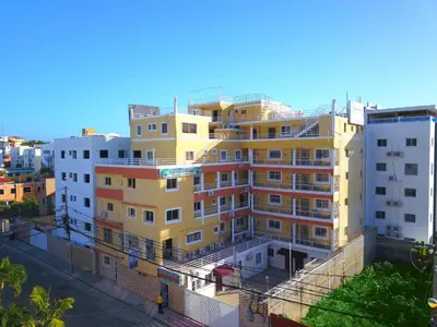 a tall yellow building in front of a city at 1 Bedroom Apartment -Corales del Sur Ole Las Americas- Isabelita - Aeropuerto in La Viva