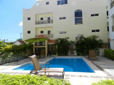a swimming pool with a chair and an umbrella next to a building at Vanilla House in Bayahibe