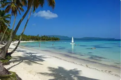 a beach with a sail boat in the water at Yes Papa! Rooms only 100m from the beach! in Las Galeras