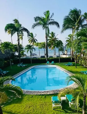 a large swimming pool with palm trees and the ocean at La Dolce Vita Beachfront Apt 2 in Las Terrenas