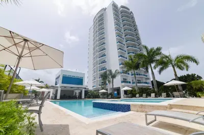 a hotel with a swimming pool and a tall building at Sunset View 2BR Apartamento Juan Dolio Las Velas in Juan Dolio
