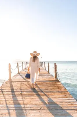 a woman walking down a wooden pier near the ocean at Punta Rucia Lodge Hotel Boutique & Spa in Punta Rucia