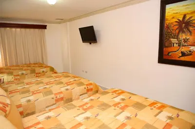 a bedroom with two beds and a tv on the wall at Hotel Los Jardines in Santiago de los Caballeros