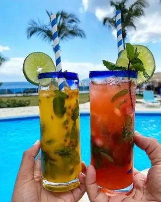 a person holding two drinks in their hands next to a pool at Tritón Hotel Boutique & Restaurant in Guayacanes