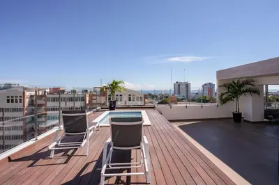 a rooftop deck with chairs and a pool on a building at Escape Apartments, Balcony, Pool & Gym in La Julia in Santo Domingo