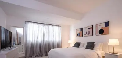 a white bedroom with a bed and a television at Apartments in La Julia 1 and 2 Bedrooms in Santo Domingo