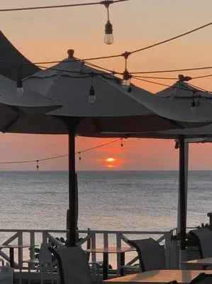 a sunset on the beach with chairs and an umbrella at Bungalow #12 at Waterfront Playa Alicia in Sosúa