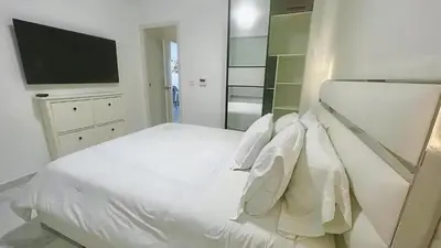 a white bedroom with a white bed and a tv at Cana Rock Star Pool View Whith BBQ in Punta Cana