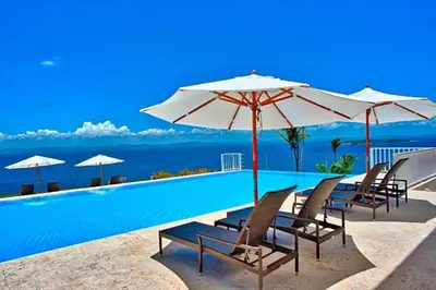 a pool with chairs and umbrellas and the ocean at Spectacular Ocean View Spacious 2-Bedroom Condo, Vista Mare, Samana DR in Santa Bárbara de Samaná
