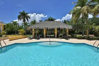 a swimming pool with a straw umbrella and palm trees at Four Points by Sheraton Santo Domingo in Santo Domingo