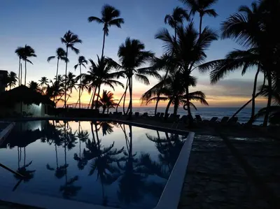 a resort swimming pool with palm trees and the ocean at Modern, Welcoming Studio, Ocean View in Juan Dolio in Juan Dolio