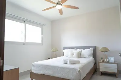 a white bedroom with a bed with a ceiling fan at Soha suites I in Santiago de los Caballeros