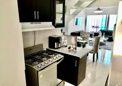 a kitchen with a stove top oven next to a living room at Acogedor apartment , seguridad las 24 horas , Cibao International Airport 8 minutos, Centro de Santiago 10 Minutos , Tamboril la capital mundial del cigarro 10 minutos in Licey al Medio