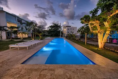 a large blue swimming pool with benches and a building at Amazing ocean view apartment with grand pool in Cabarete