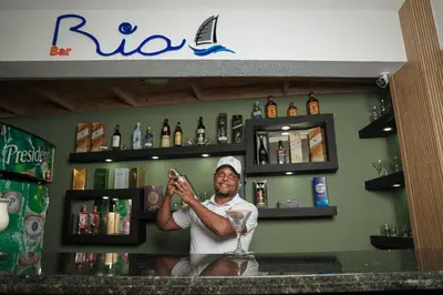 a man standing behind a bar holding a wine glass at Ria Hotel in San Felipe de Puerto Plata
