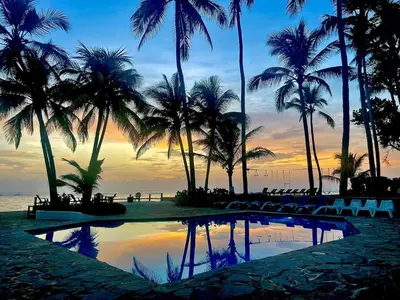 a sunset at the beach with palm trees and a pool at Studio Beachfront Kite Beach in Cabarete