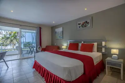 a bedroom with a bed with red pillows and a balcony at Costarena Beach Hotel in Las Terrenas