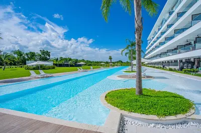 a swimming pool with a palm tree in front of a building at Xeliter Cana Rock Punta Cana in Punta Cana