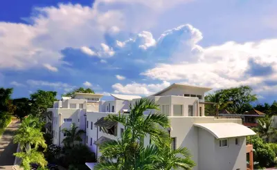 a white building with palm trees in front of it at Infiniti Blu Luxury Ocean Front Condos in Sosúa