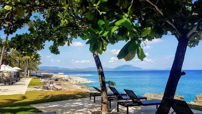 a view of the ocean from a beach with chairs and trees at Infiniti Blu Luxury Ocean Front Condos in Sosúa