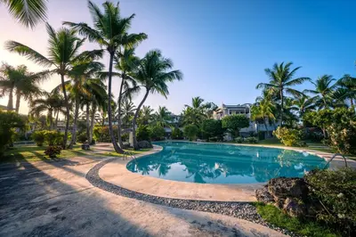 a pool with palm trees and a house in the background at Family Dominicus Apartment - Bayahibe in Bayahibe