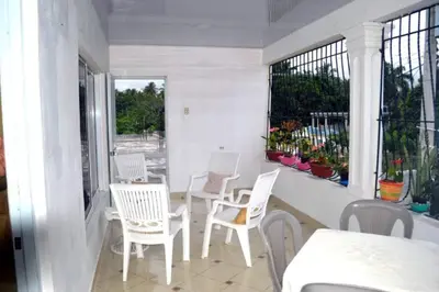 a porch with white chairs and tables and windows at Alojamiento Wilkenia in Ochoa