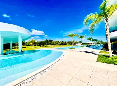 a swimming pool with palm trees and a building at Luxury Apartment With Pool And Golf View in Punta Cana