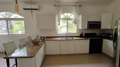 a kitchen with white cabinets and a sink and two windows at Luxury 4-Bedroom Villa with Climate Pool in Sosúa
