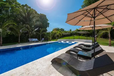 a swimming pool with chairs and an umbrella at Luxury 4-Bedroom Villa with Climate Pool in Sosúa