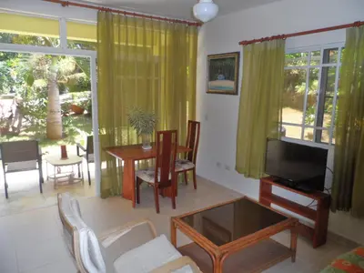 a living room with a television and a table and chairs at Costambar Tropical Garden in San Felipe de Puerto Plata