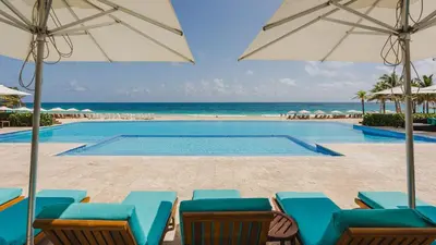 a pool with chairs and umbrellas and the ocean at Hard Rock Golf Cozy 1BR • Pool & Golf Views in Punta Cana