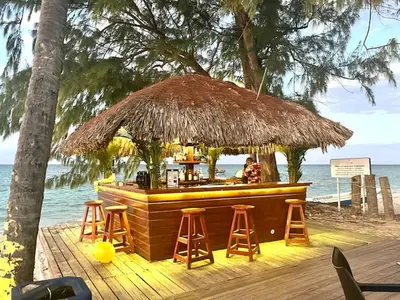 a bar on the beach with stools and a straw umbrella at Chic Beachfront Apartment - Private Beach Access in Punta Cana
