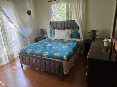 a bedroom with a bed with a blue comforter and a window at Hacienda Claro de Luna 3 Bedrooms in Jarabacoa