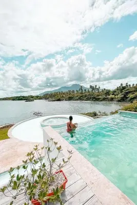 a man in a swimming pool next to a body of water at Peninsula Esmeralda Luxury Hotel & Villas in San Felipe de Puerto Plata