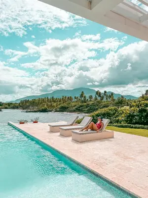 a woman sitting on a chair next to a swimming pool at Peninsula Esmeralda Luxury Hotel & Villas in San Felipe de Puerto Plata