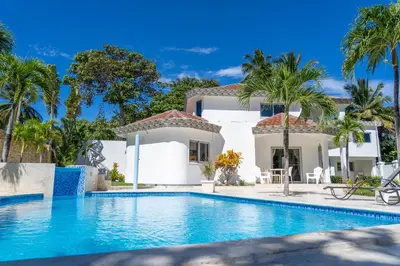a swimming pool in front of a house with palm trees at Casa Blanca - White House in Cabarete