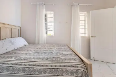 a bed in a white room with two windows at The Green Palms 5 Bedroom villa with pool / garden in San Felipe de Puerto Plata