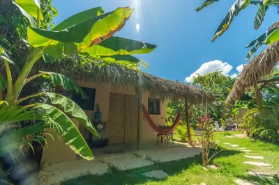 a small house with a thatch roof and a chair at Casita Chinola - Playa El Encuentro in Bombita