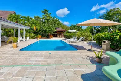 a swimming pool with an umbrella and a house at Río Mar Cumayasa in La Romana