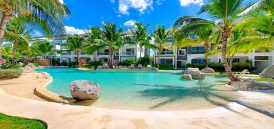 a swimming pool with palm trees in front of a building at Caribbean Star - Estrella Dominicus Bayahibe in Bayahibe