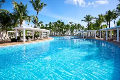 a large swimming pool with chairs and palm trees at Riu Palace Bavaro - All Inclusive in Punta Cana